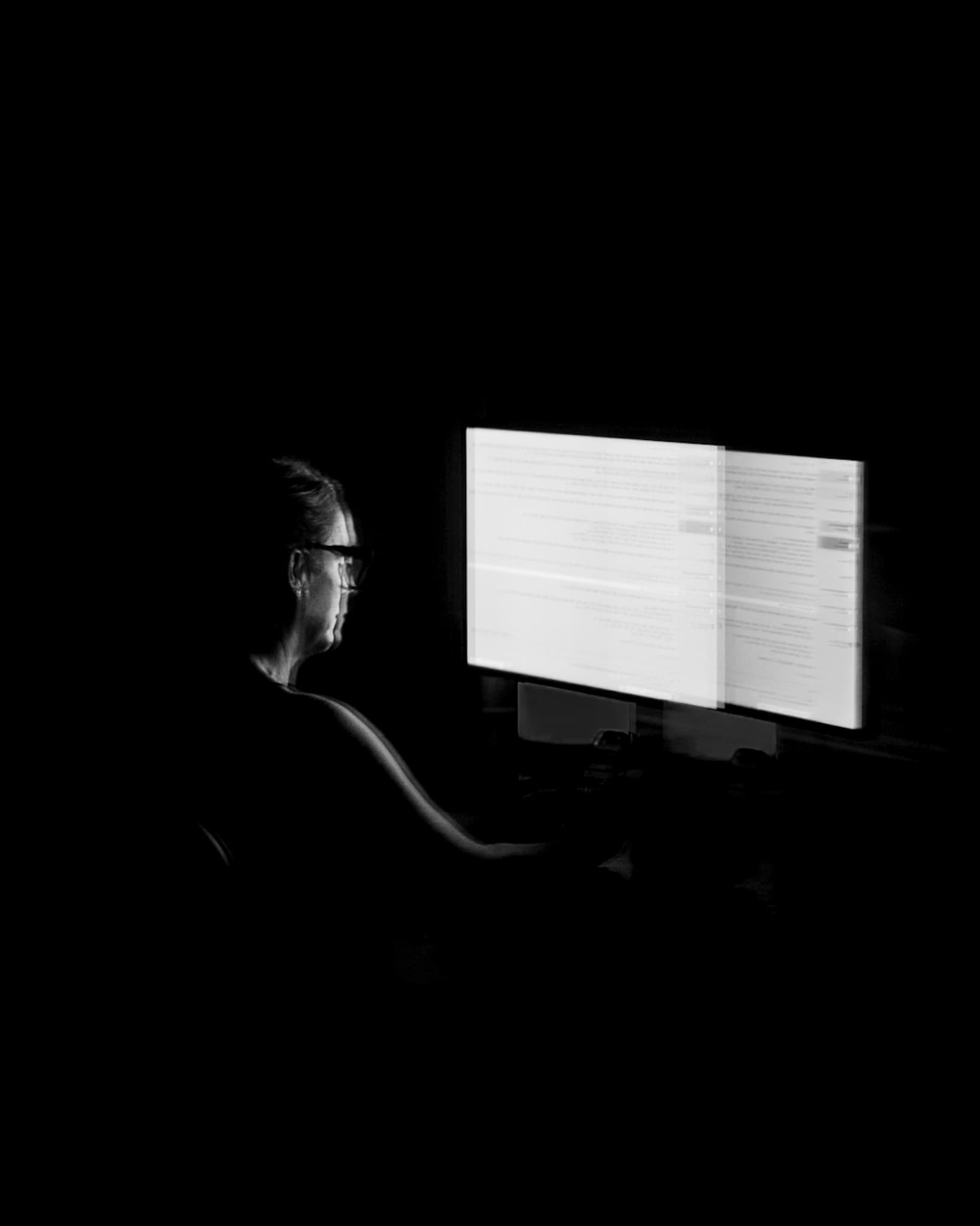 A person working at illuminated monitors in a dark room